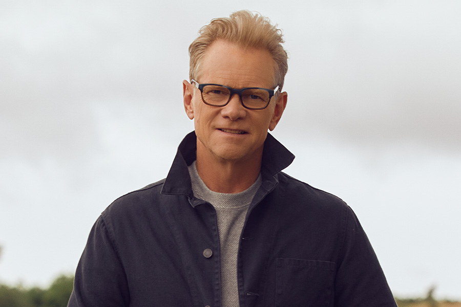 Man with blond hair, wearing glasses and a jacket - sky behind him